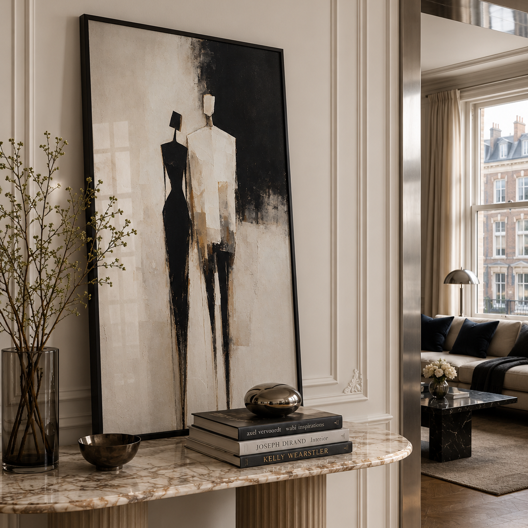 A large framed abstract art print featuring two minimalist fashion mannequins in black, white, and beige tones, displayed on a marble console table in a classic European-style living room.