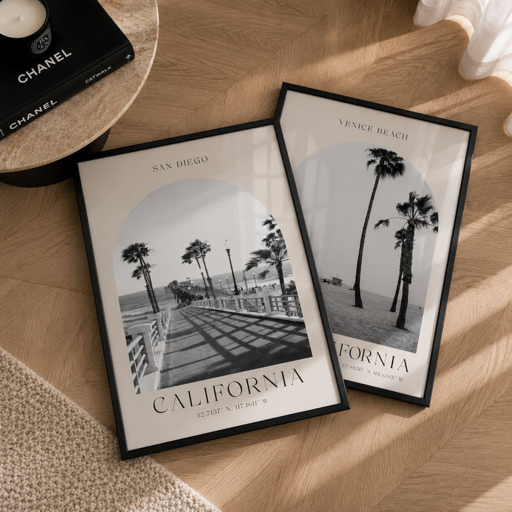 Two framed prints of beach scenes with palm trees on a wooden surface.