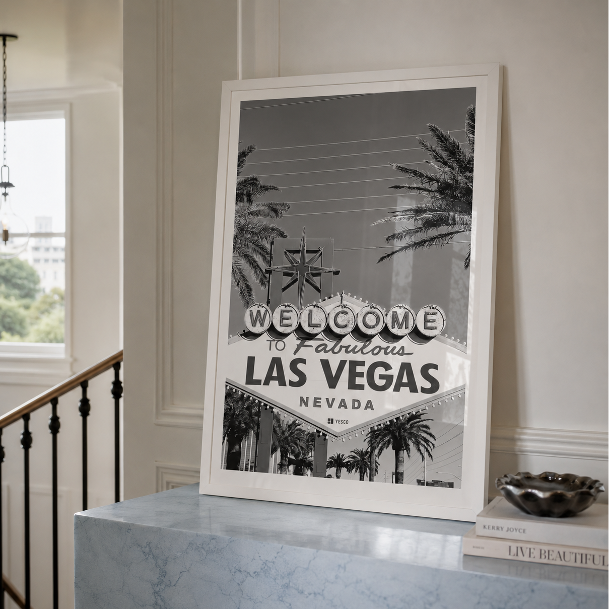 A framed black and white art print of the 'Welcome to Fabulous Las Vegas Nevada' sign, leaning on a light blue marble console table in a modern, elegant interior setting.