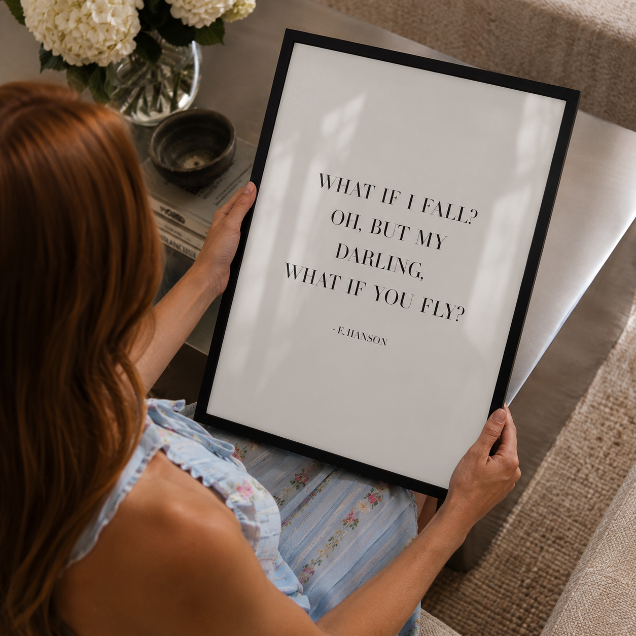 A woman holds a black-framed art print featuring the quote 'WHAT IF I FALL? OH, BUT MY DARLING, WHAT IF YOU FLY?' attributed to E. Hanson.
