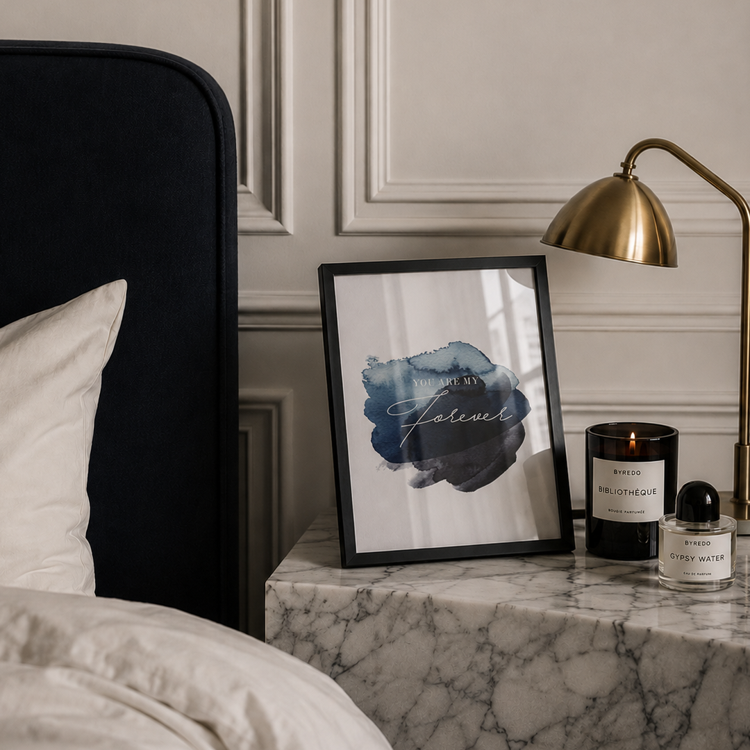 Marble nightstand with framed artwork, candle, and lamp in a bedroom setting.